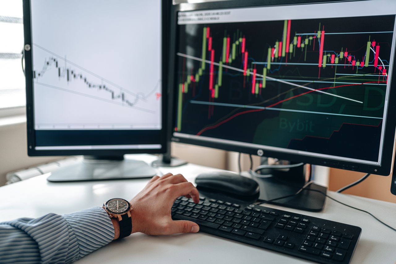gallery-5 A businessperson using dual monitors to analyze stock market trends with charts and graphs.