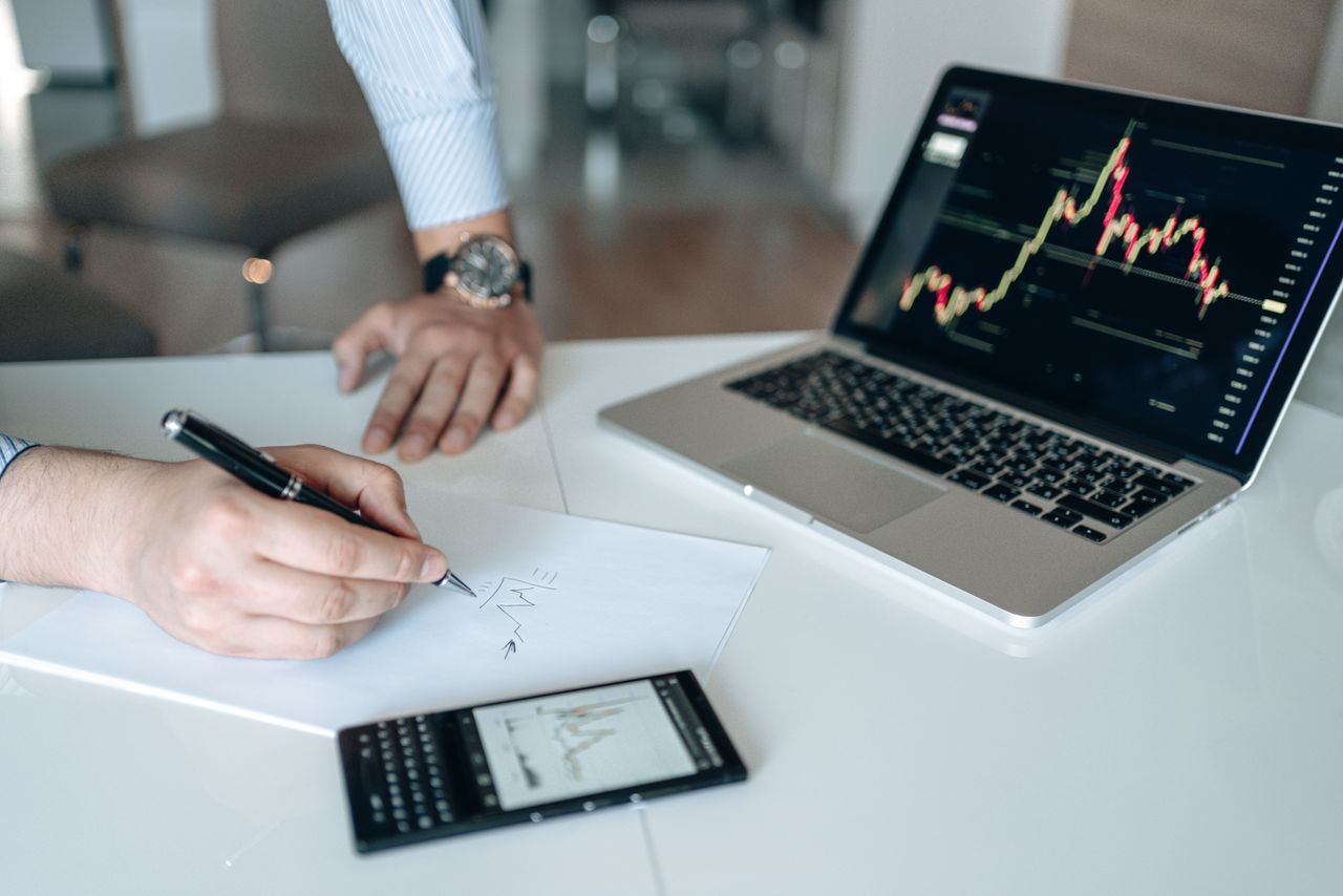Professional workspace featuring laptop with stock charts, smartphone, and paper for business analysis.