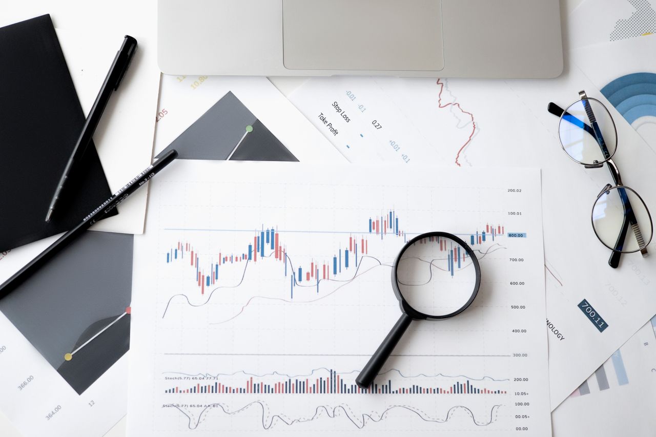 gallery-3 Flat lay of stock market analysis documents with magnifying glass, pens, and glasses.